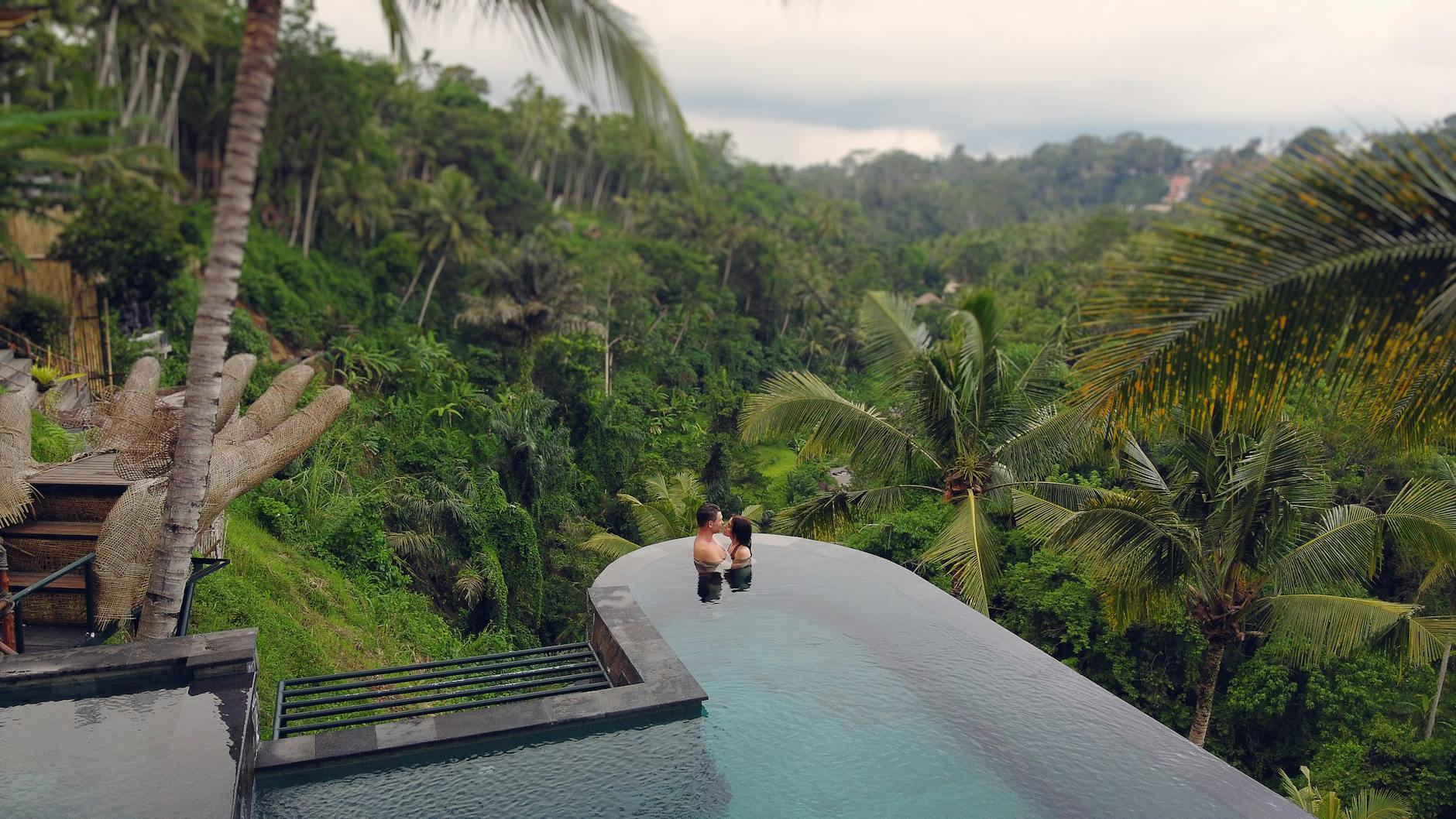 Romantic couple relaxing in infinity pool with tropical Bali landscape views on honeymoon