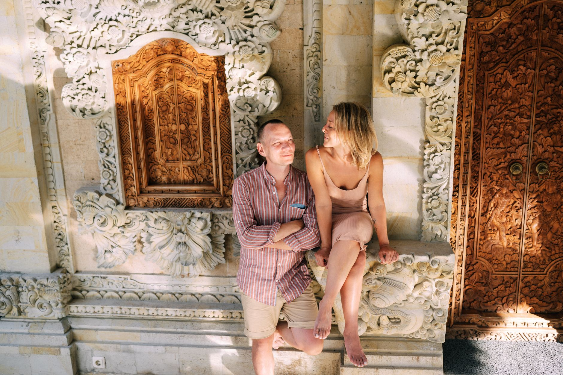 Couple relaxing by ornate Balinese temple wall enjoying sunlight and cultural romance Bali