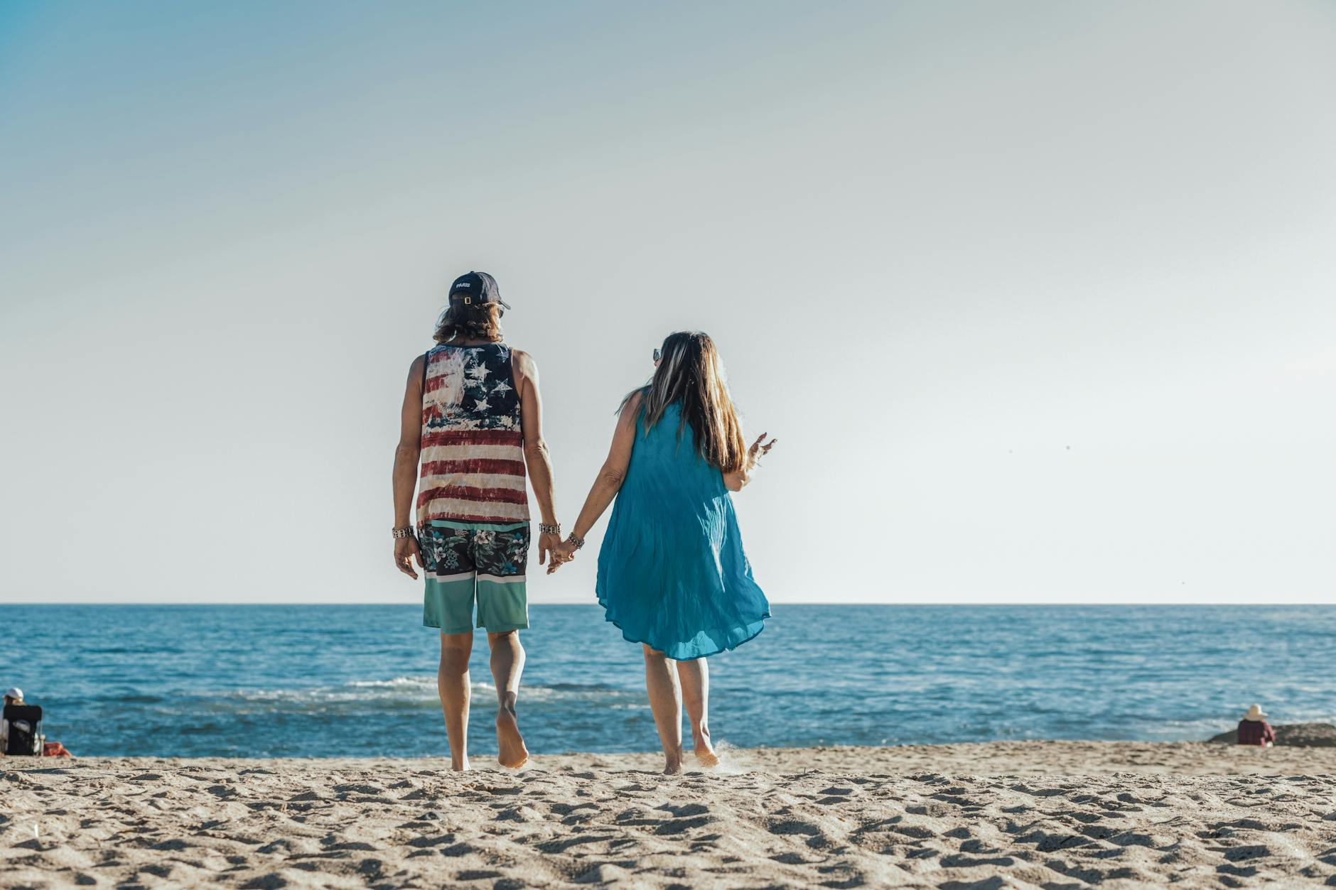 Happy couple holding hands walking on sandy beach under clear blue sky romantic vacation