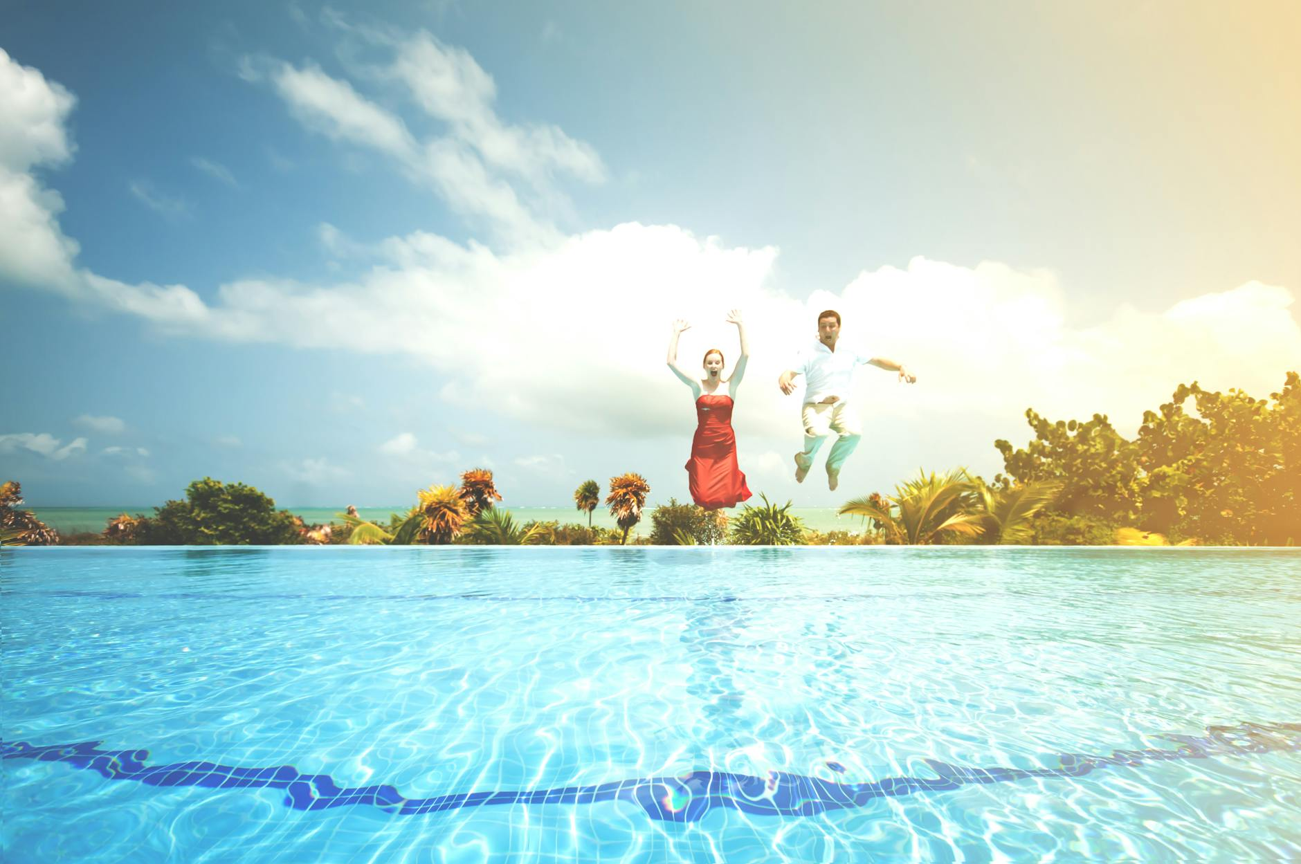 Couple jumping into pool surrounded by palm trees at luxury Mexico tropical resort