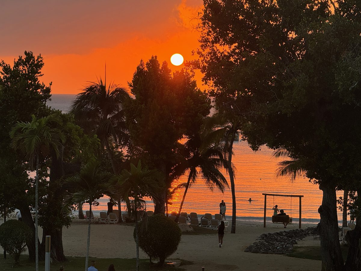 Sunset over the beach at Negril, Jamaica, with palm trees and couples silhouetted