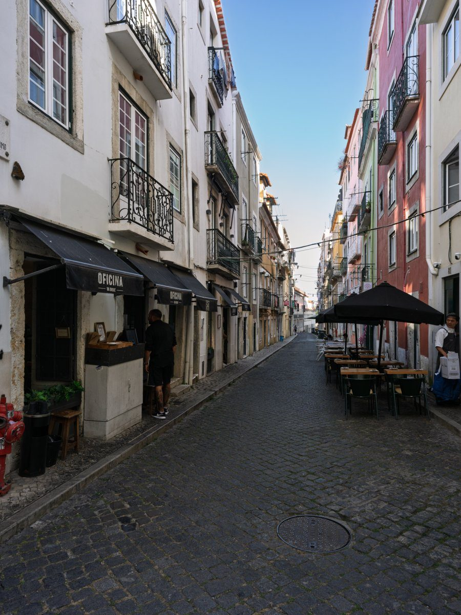 A narrow cobblestone street lined with colorful buildings and outdoor cafes in Lisbon, Portugal