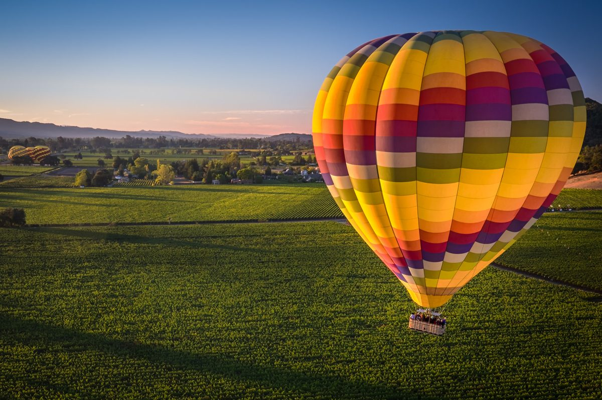 A hot air balloon flying over vineyards in Napa Valley, California, at sunrise