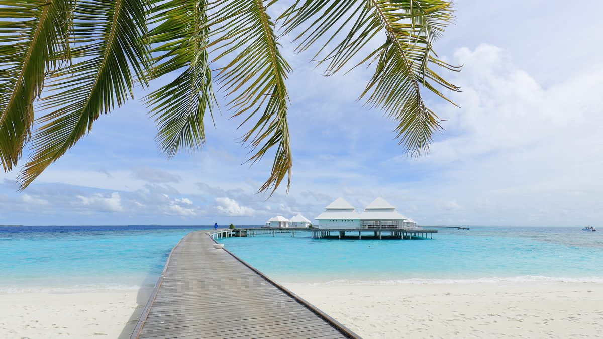 Overwater villas connected by a wooden walkway above a turquoise Maldives lagoon